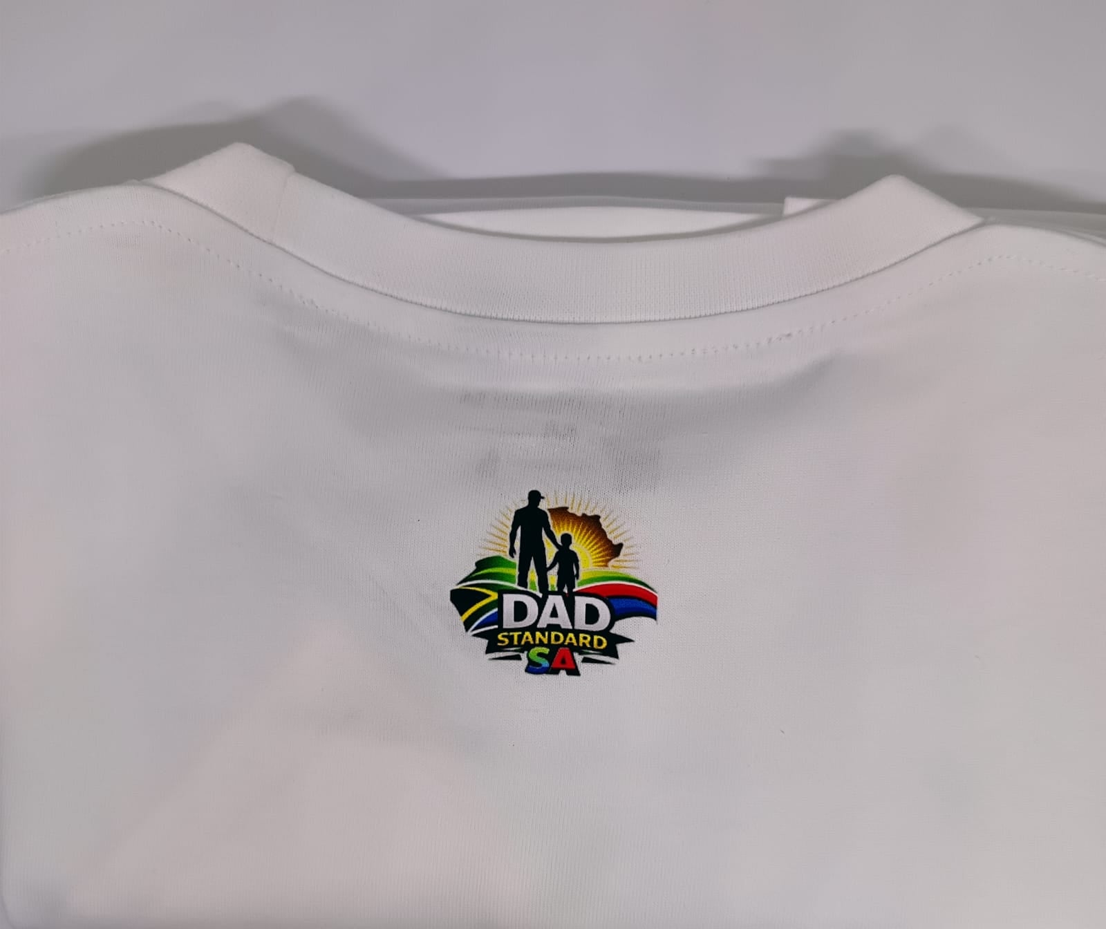White t-shirt with a colorful 'DAD Standard' logo on a light gray background